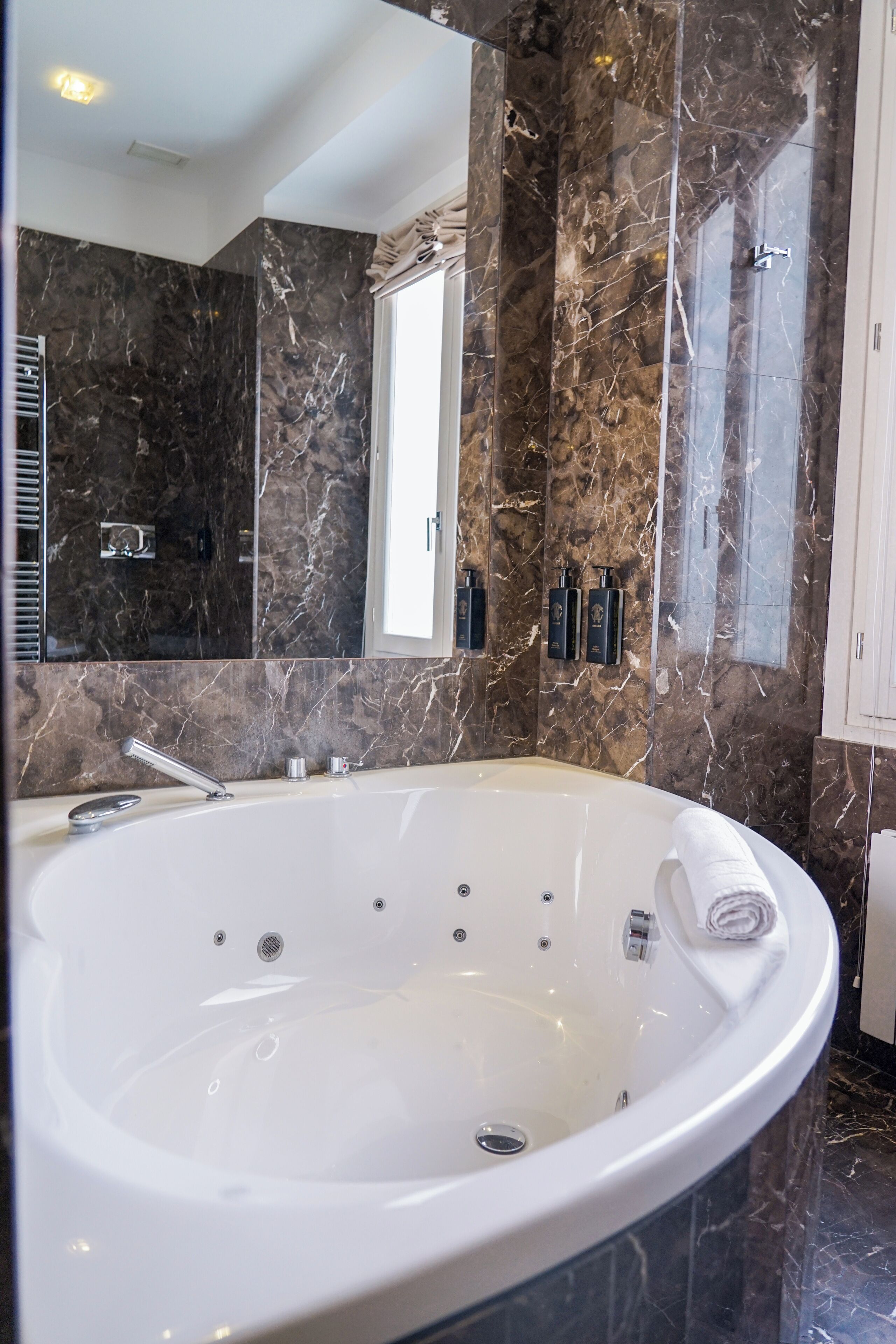 A modern bathroom with a large bathtub, marble walls, and a large mirror.