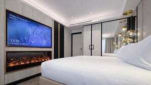 Une chambre d’hôtel moderne dotée d’une grande télévision à écran plat, d’une cheminée, d’un grand lit et d’un lustre élégant.
