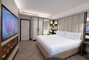 A modern hotel room with a large bed, a flat-screen TV, a fireplace, and a mirror.