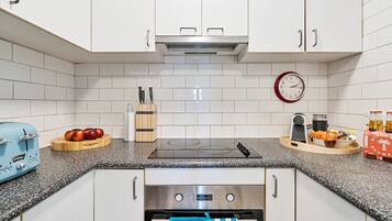 A modern kitchen with white cabinets, a stainless steel range hood, a built-in oven, a clock, and a coffee machine.