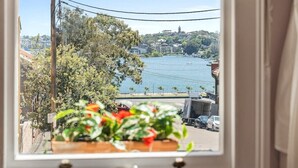 Vista desde una ventana sobre un cuerpo de agua, con un puente, árboles y edificios al fondo.
