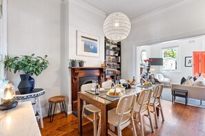 Un comedor con una mesa de madera, sillas de mimbre, una araña y una estantería.