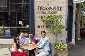 Un grupo de personas sentadas en una mesa al aire libre frente a un edificio con un letrero que dice 'BRASSEERIE 1st FLOOR BREWERY HOTEL'.