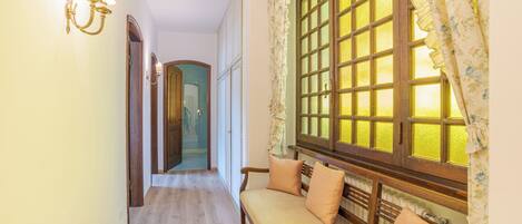 A hallway with a wooden bench, a wall-mounted light fixture, and a window with floral curtains.