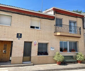 A two-story building with a brick facade, a balcony with a metal railing, and a door with a window.