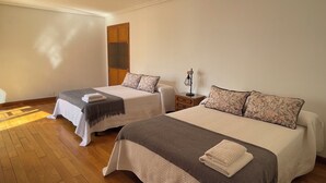 Habitación de hotel con dos camas, suelo de madera, un armario y una mesita de noche con lámpara.