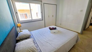 A bedroom with a bed, a bedside table with a lamp, a window, and a wardrobe. - Modern Retreat: 2br Stylish Apt with Comfy Rooms! (Larnaca)