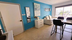 Een moderne woonkamer met een blauwe wand, een witte bank, een eettafel met stoelen en een groot raam.