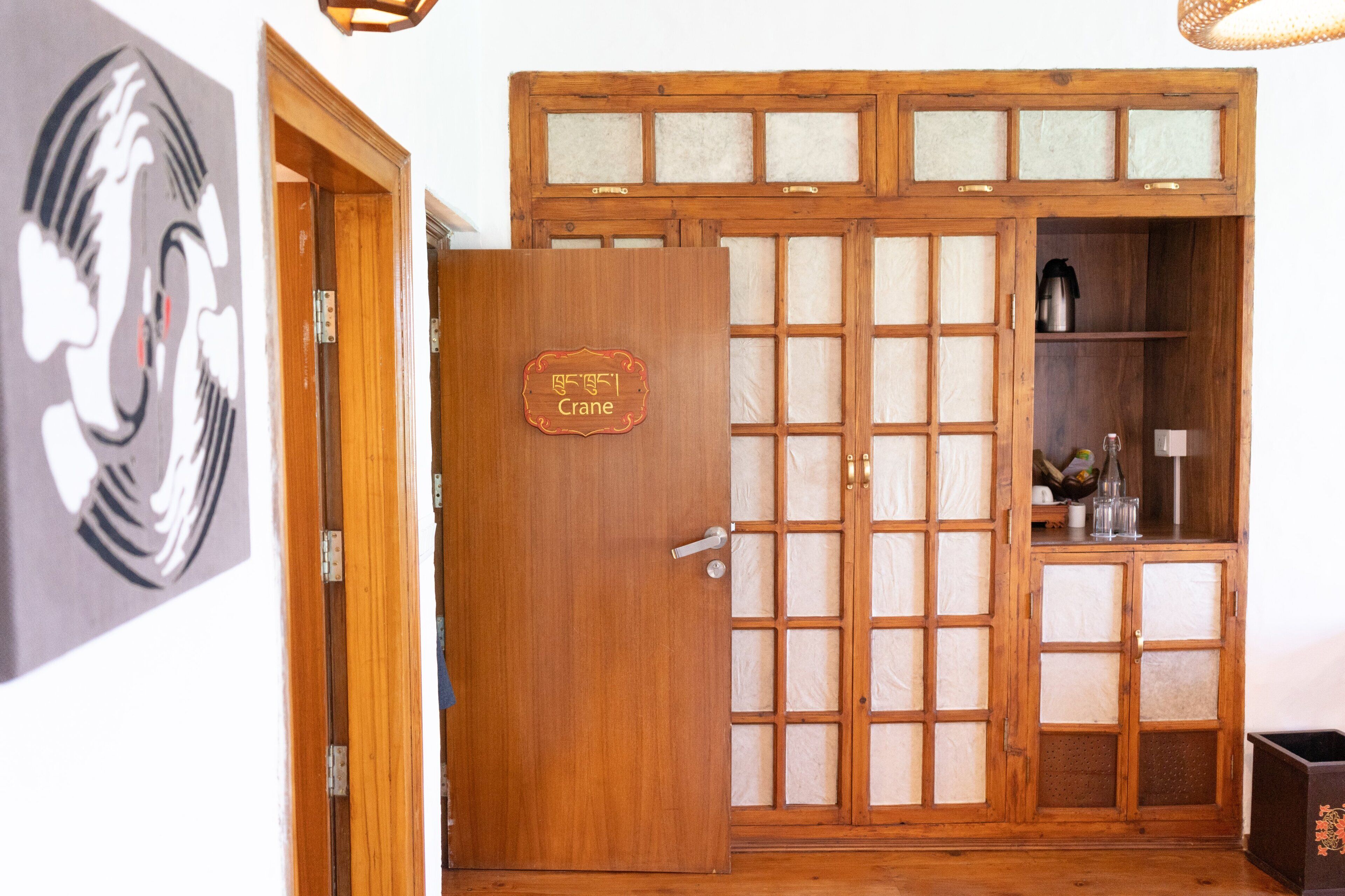 A traditional wooden door with a sign reading "Crane" and a wooden cabinet with glass panels and a shelf with items.