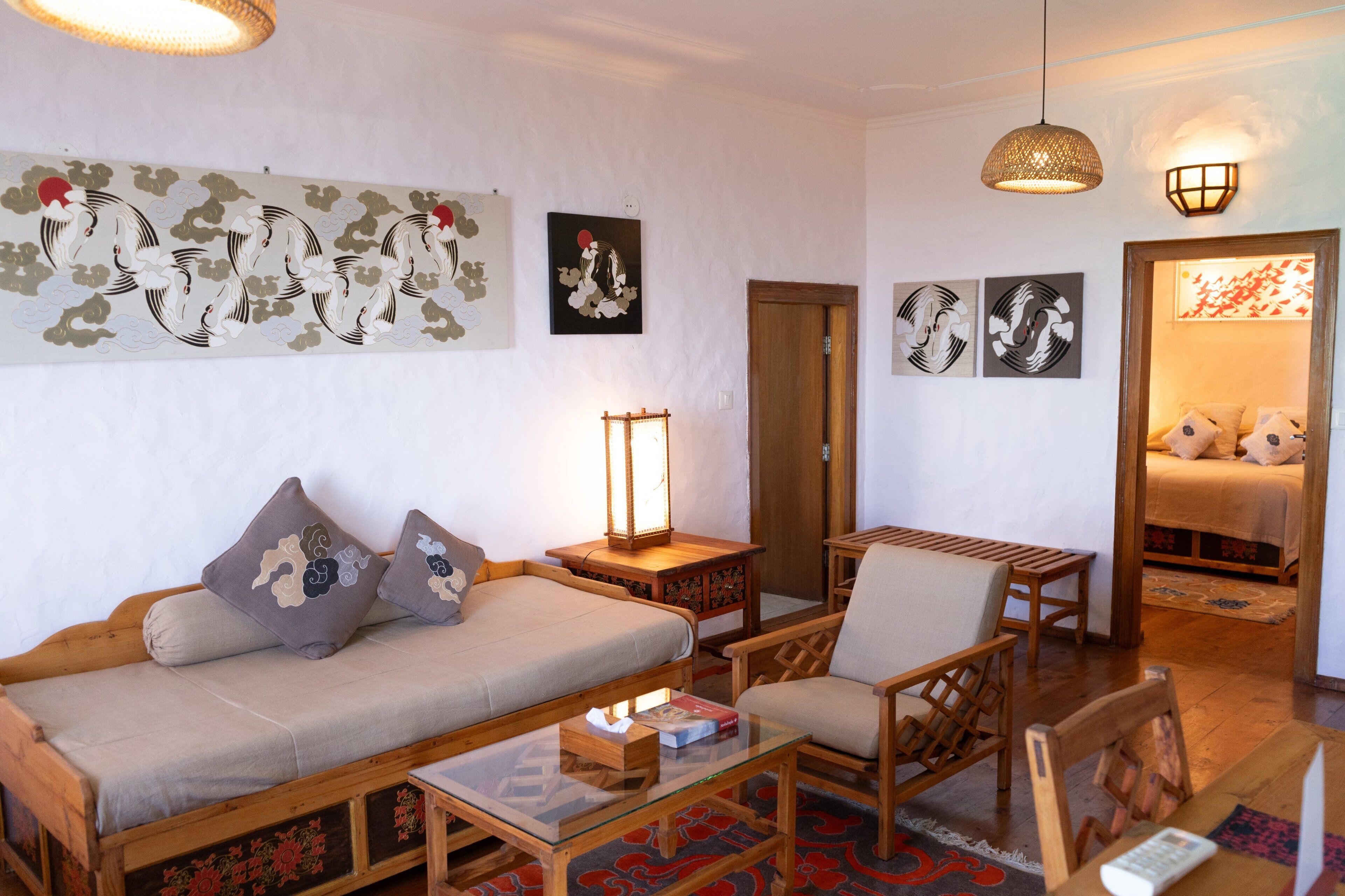 A traditional Japanese-style room with tatami flooring, a low wooden bed, a sofa with cushions, a wooden table, and a hanging lantern.