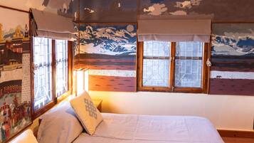 Ein Schlafzimmer mit einem Bett, einem Fenster mit Vorhängen und einer Wand mit einer gemaltem Landschaftsbild.