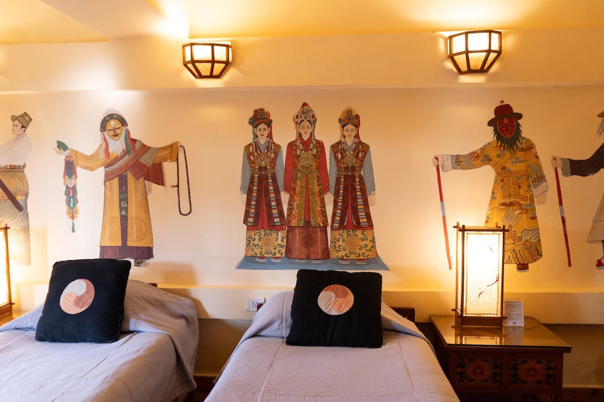 A hotel room with two beds, a wall mural, and a traditional Chinese lantern.