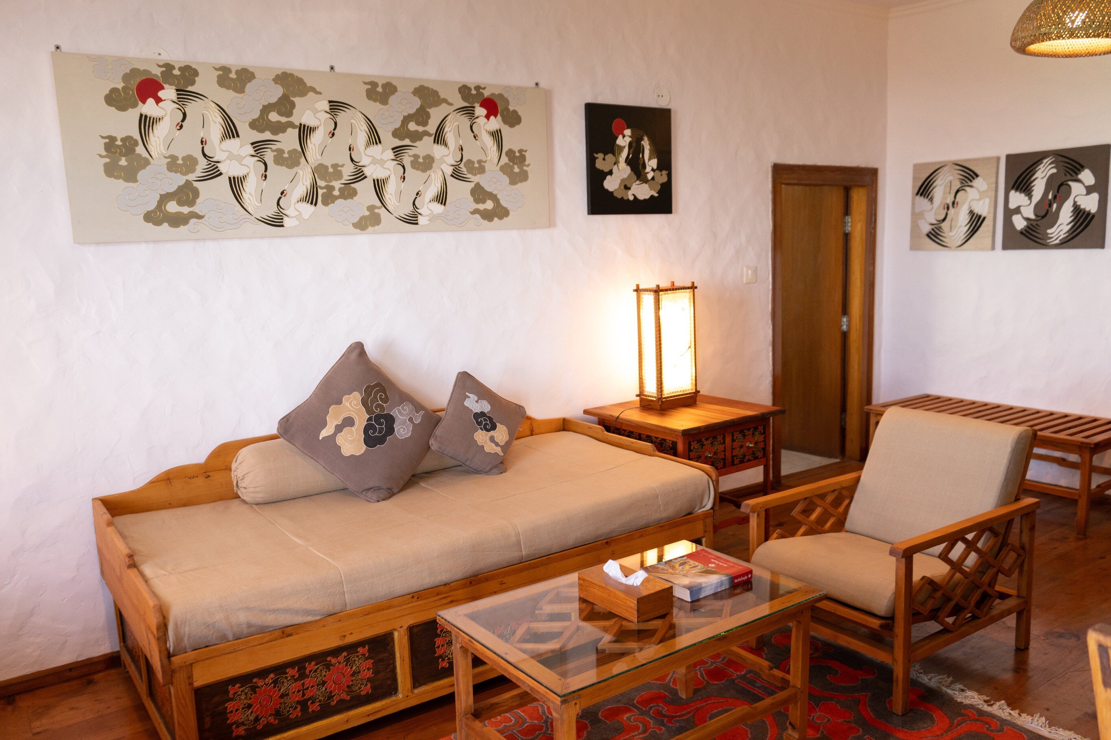 Una habitación de estilo japonés tradicional con una cama de madera baja, una silla de madera, una mesita de centro de vidrio y obras de arte en las paredes.