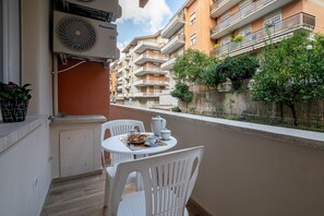 A balcony with a table set for two, a white chair, and a ceiling fan.