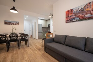 Una sala de estar moderna con un sofá gris, una mesa de comedor con sillas, una mesita auxiliar y un cuadro en la pared.