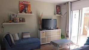 Un salon avec un canapé bleu, une table basse, un téléviseur posé sur un meuble et une affiche accrochée au mur.