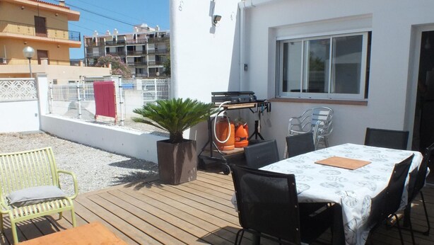 Une terrasse extérieure avec une table et des chaises, un barbecue et une plante en pot.