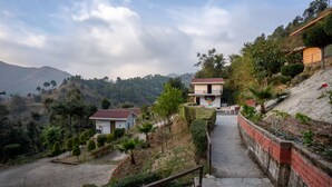 Una propiedad en una ladera con un camino pavimentado que lleva a una casa de techo rojo.