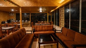 Un interior acogedor con techo y paredes de madera, un comedor con mesas y sillas, y ventanas grandes con diseños decorativos.