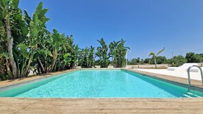 Ein rechteckiger Pool mit klarem, blauem Wasser, umgeben von üppiger tropischer Vegetation und einer Holzterrasse.