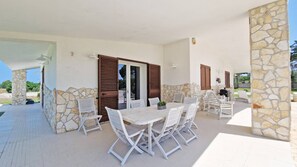 Eine Terrasse im Freien mit einer Steinwand, weißen Möbeln und Holzläden.