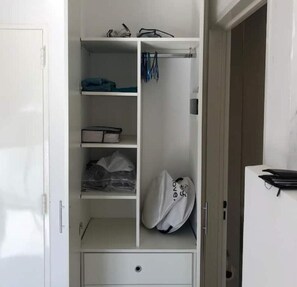 Un armario blanco con estantes, espacio para colgar, un cajón pequeño y una puerta con tirador.