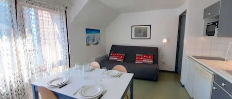 A compact living space with a dining area, kitchenette, and a sofa with decorative pillows.