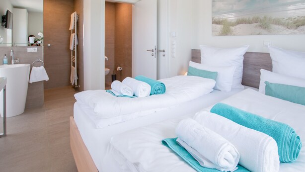 A hotel room with a large bed, a bathroom, and a painting of a beach scene. - Modernes Ferienhaus in Attraktiver Lage in Burhave. Strandnah und Zentral (Burhave)
