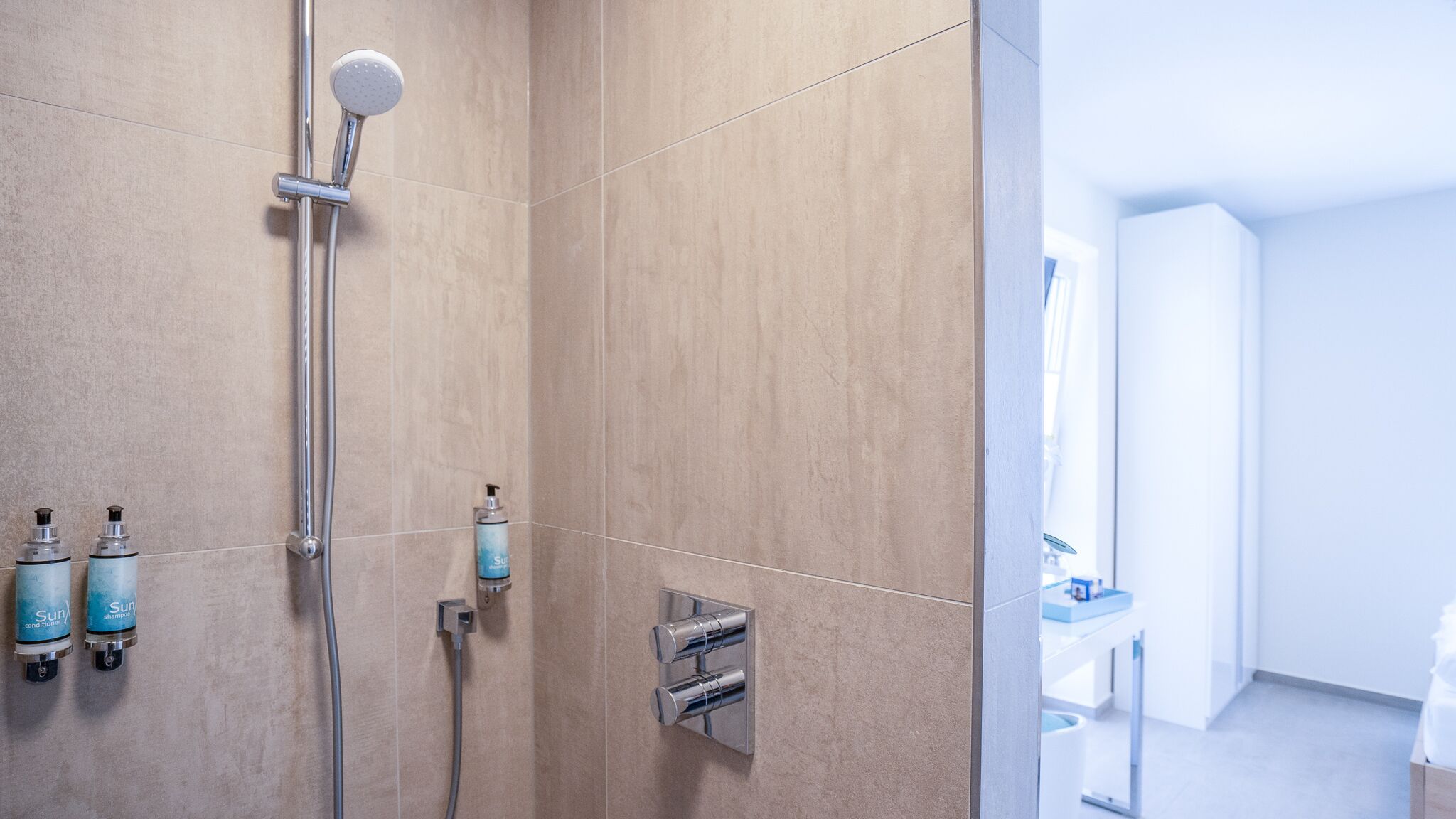 Een moderne badkamer met een douche, twee flesjes Sun conditioner en een handdouche.