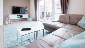 A modern living room with a sofa, a TV mounted on the wall, and a sliding glass door leading to an outdoor area. - Modernes Ferienhaus in Attraktiver Lage in Burhave. Strandnah und Zentral (Burhave)