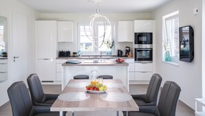 A modern kitchen with white cabinets, a built-in oven, and a large island with a sink. - Modernes Ferienhaus in Attraktiver Lage in Burhave. Strandnah und Zentral (Burhave)