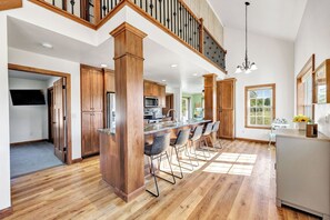 Eine geräumige Küche mit Holzausbau, einer zentralen Kochinsel mit Barhocker und einer Treppe, die in einen oberen Bereich führt.
