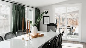 A dining area with a white table, black chairs, a large vase, and a wooden tray. - Designer Home with HotTub, Movie Room, Firepit (Arvada)
