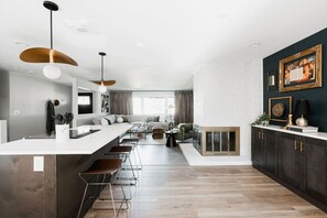 A modern kitchen with a central island, pendant lighting, and a dark-colored cabinet with gold handles. - Designer Home with HotTub, Movie Room, Firepit (Arvada)