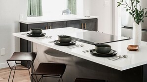 A modern kitchen with a central island, black stools, and a minimalist design. - Designer Home with HotTub, Movie Room, Firepit (Arvada)