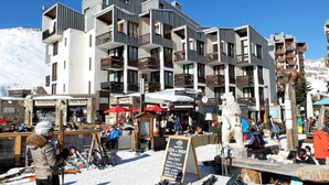 Ein modernes Mehrstöckiges Hotel mit Balkonen, Skiausrüstung und Sitzgelegenheiten im Freien.