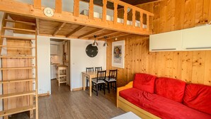 Ein Holzinnenraum mit einem Schlafplatz auf Lade, einem roten Sofa, einem Esstisch mit Stühlen und einem weißen Tisch.