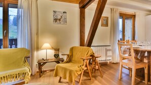 A cozy room with a wooden floor, a dining table set for four, a yellow armchair, a lamp, and a painting on the wall. - Charming Apartment for 6 in the Heart of Les Gets Village, Close to Slopes (Les Gets)