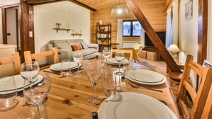 A dining area with a wooden table set for a meal, a sofa, and a bookshelf in a room with wooden beams and white walls. - Charming Apartment for 6 in the Heart of Les Gets Village, Close to Slopes (Les Gets)