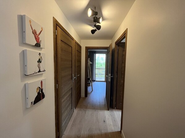 Un couloir avec des portes en bois, un luminaire au plafond et une vue sur un balcon extérieur.