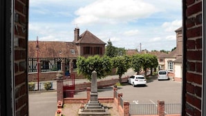 Une rue résidentielle bordée de maisons en briques, avec un monument central et des voitures garées.