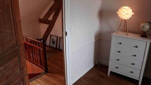 Un escalier avec des rampes en bois mène à un mur blanc. On y trouve une table de chevet blanche, dotée de tiroirs, et un globe terrestre posé sur le dessus.