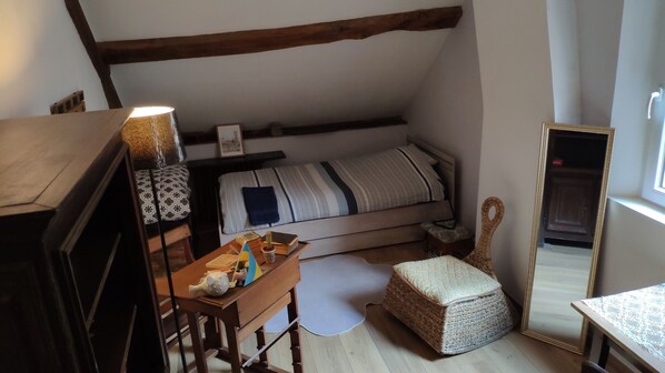 Un dormitorio acogedor con cama, cómoda de madera, mesita con objetos decorativos, pouf tejido y espejo.