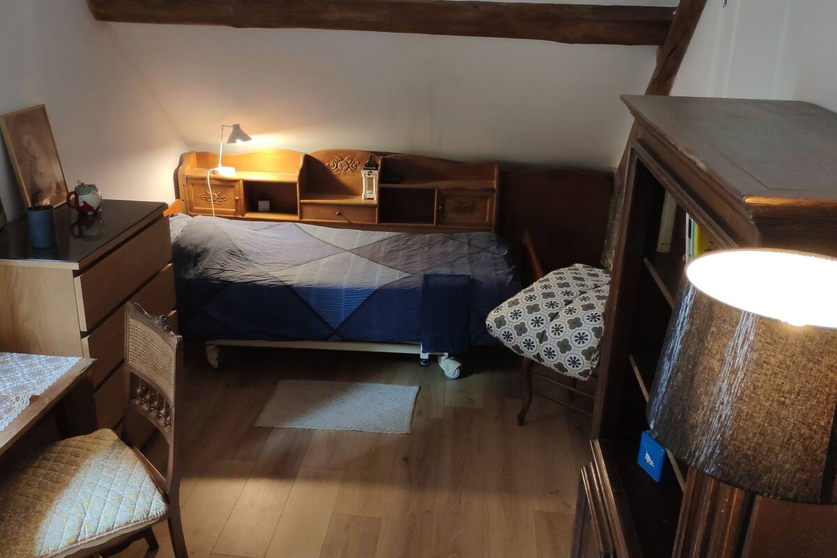 Ein kleines, gemütliches Schlafzimmer mit Bett, Schreibtisch, Stuhl und Lampe.