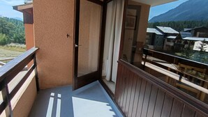 Een balkon met een houten hekwerk, een schuifdeur en uitzicht op een bergachtig landschap.