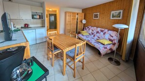 Een knus woongedeelte met een kitchenette, een eettafel, een bank en een vloerlamp.