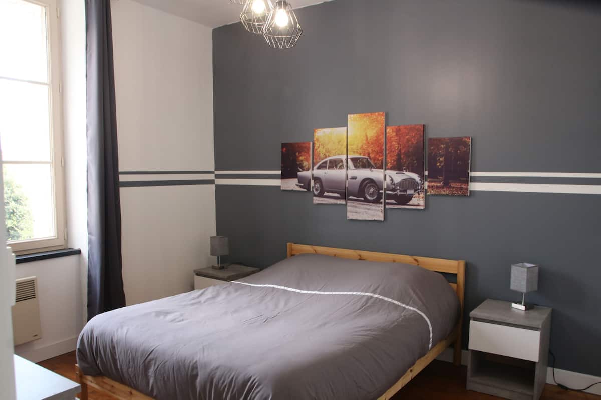A bedroom with a bed, a nightstand, a lamp, and a wall with a car-themed artwork.