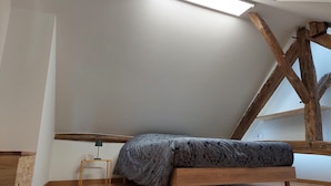 A bedroom with a sloped ceiling, a bed, a small table, and a lamp. - Le km99 (Pont-sur-Yonne)