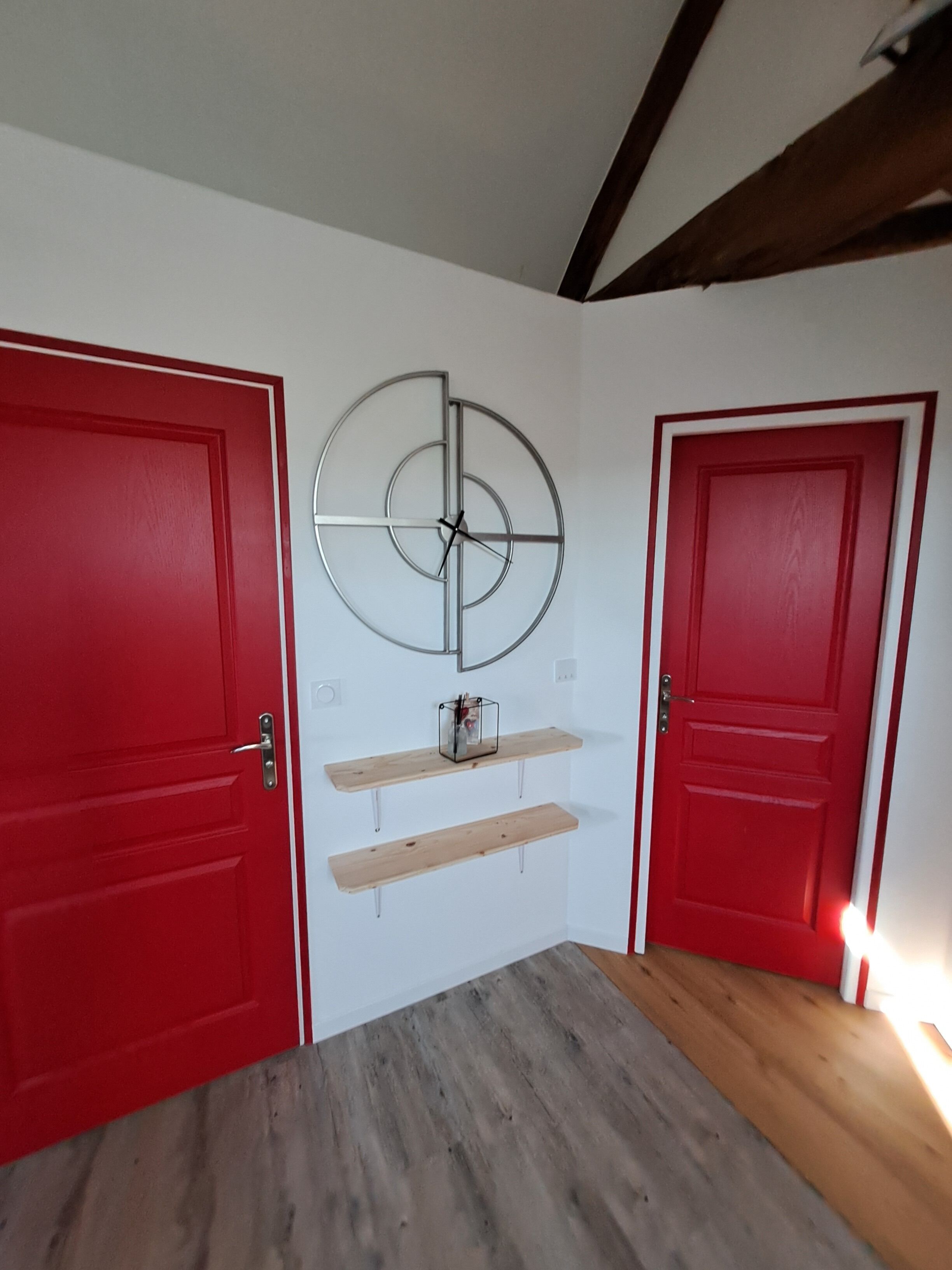 Une pièce avec deux portes rouges, un plancher en bois et une horloge fixée au mur.