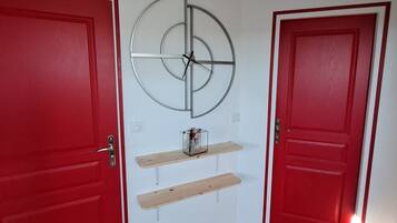 Une pièce avec deux portes rouges, un plancher en bois et une horloge fixée au mur.